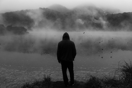 A man in a hood stands in the background of the river with fog and flying swallowsの写真素材