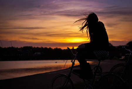 Silhouette of a girl sitting on a bike at sunsetの写真素材