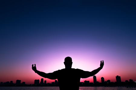 Silhouette of a man stretched out his hands, on background of sunset cityの写真素材