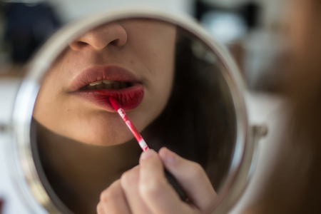 Girl paints her lips, reflected in a round mirrorの写真素材