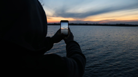 Girl photographs on a mobile phone lakeの写真素材