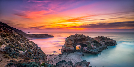 The fiery sky during sunset on the beach near the rocksの写真素材