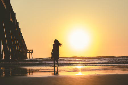 Silhouette of woman in dress walking on the sea beach at sunsetの写真素材