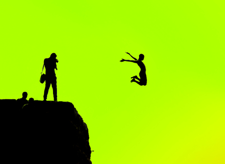 Silhouette of a man jumping off a cliff on a green backgroundの写真素材