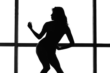 Silhouette of a woman posing in a piquant pose against a white glassの写真素材