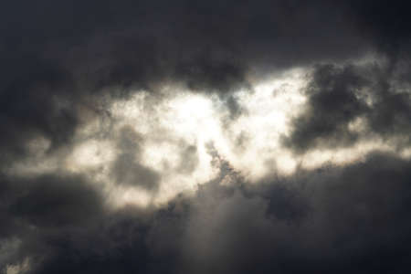 Black sky with gray and black stormy clouds and sunshine coming through