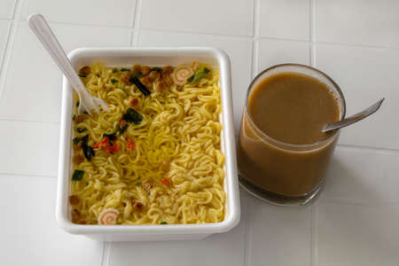Instant noodles in a plastic box and a glass of coffee. Fast breakfast.