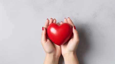 Female hands holding a red heart on a gray background, top viewの素材