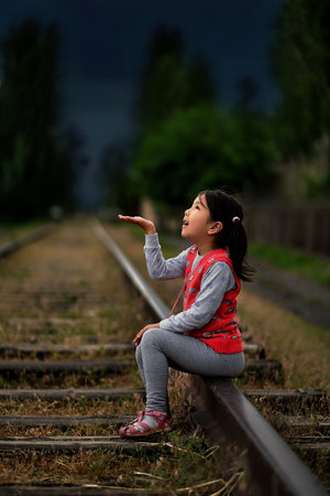 A little girl sits on the rails, extending her palm to catch the drops of spring rain.の写真素材