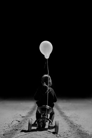 Black and white image of a child with a balloon on the road.