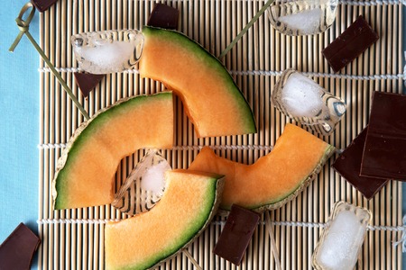 Slices of melon on skewers with dark chocolate on a bamboo matの写真素材