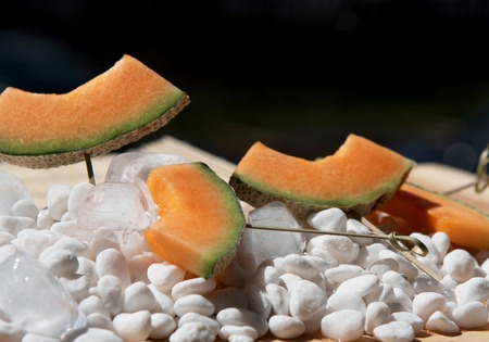 Slices of melon on skewers on white stonesの写真素材