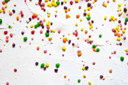 Rainbow colored candy sprinkled on a white background.