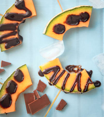 Summer dessert Slices of melon with dark chocolate on skewers. Healthy dessert.の写真素材