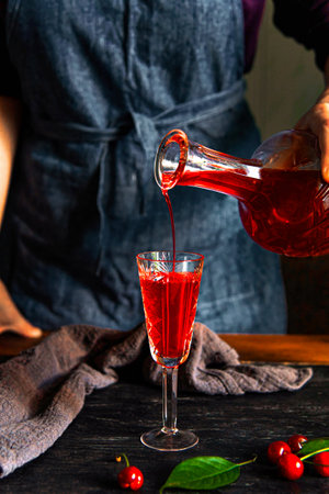 A woman's hand pours cherry liqueur into a glass. Homemade cherry liqueur.の写真素材