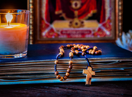 The time for prayer. Wooden Rosary on an ancient prayer book. Icon of the Mother of God and Jesus. Lighted candle.の写真素材