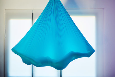 Blue hammock hanging on the wall in the room, with a silhouette of a woman relaxing while she does flying yogaの写真素材