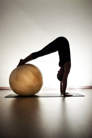 Woman practicing yoga in a studio with a pilates ball, silhouetteの写真素材