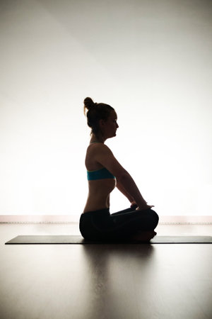 Young woman practicing yoga indoors, sitting in Ardha Padmasana exerciseの写真素材