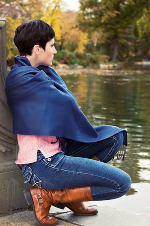 A beautiful woman sitting by the pond in a park and looking at waterの写真素材