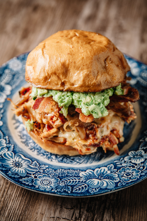 Smoked bbq chicken sandwich with sauteed onions, bacon, peper jack cheese and guacamole spread on rustic backgroundの写真素材