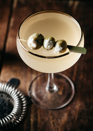 A martini garnished with stuffed olives on wooden surface, verticalの写真素材