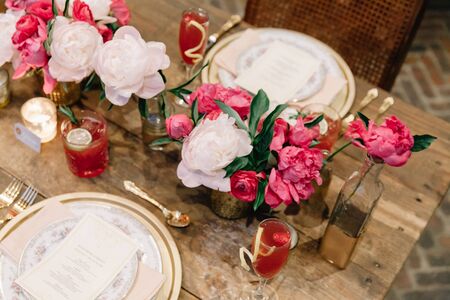 Elegant wedding table with glasses, dishes and flowers decoration indoors in a restaurant. Gorgeous rustic long wedding table. Wedding decoration concept. Pink, white and gold color paletteの写真素材