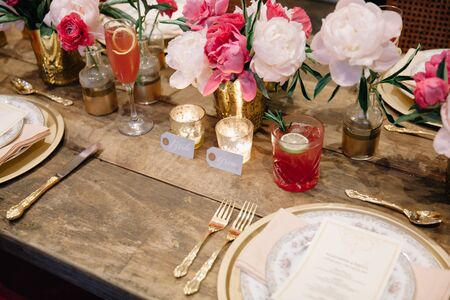 Elegant dark pink wedding banquet table with glasses, dishes and flowers decoration indoors in...