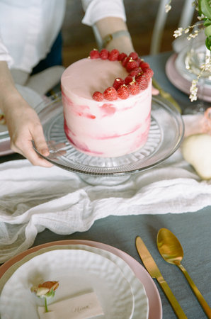Elegant dessert presentation with a pink raspberry cake on a beautifully set dining table in a cozy settingの写真素材