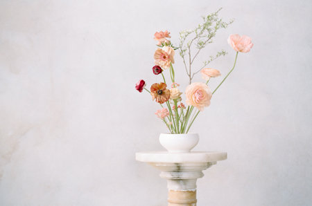 Elegant floral arrangement in a simple bowl placed on a pedestal against a soft pastel backgroundの写真素材