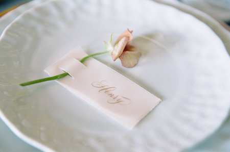 Elegant table setting featuring hand-written place card and delicate flower on fine china plate