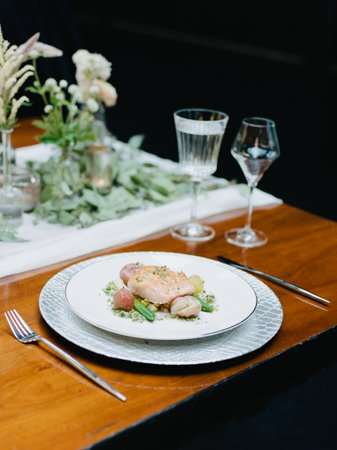 A beautifully arranged plate holds a gourmet dish accompanied by seasonal vegetables. Glasses of water and wine add to the sophisticated dining atmosphere.の写真素材