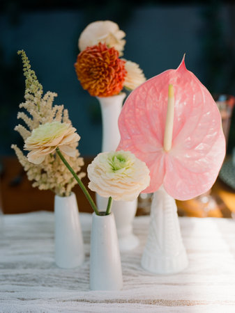 A diverse array of flowers in distinctive white vases, including vibrant blooms and lush greenery, beautifully displayed on a table in natural light.の写真素材