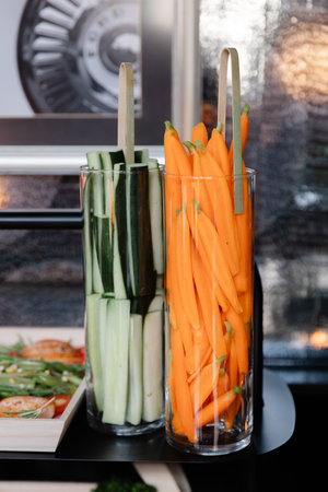 Colorful, freshly cut carrots and cucumbers are neatly arranged in transparent glass containers at an elegant dining event in a contemporary restaurant, showcasing healthy food options.の写真素材