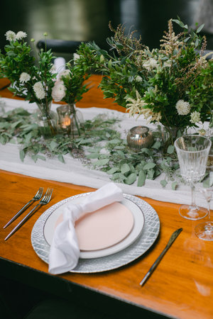 A beautifully arranged dining table showcases a pale plate, elegant cutlery, and lush green floral centerpieces. Soft candlelight adds warmth to the inviting atmosphere.の写真素材