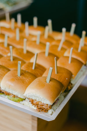 A variety of mini sandwiches are neatly arranged on a wooden platter, each filled with delicious ingredients and topped with a toothpick, perfect for a casual gathering.の写真素材
