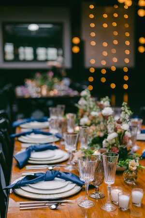 A beautifully arranged dining table features delicate floral centerpieces, elegant glassware, and soft blue napkins, set for a special gathering in a cozy space with warm lighting.の写真素材