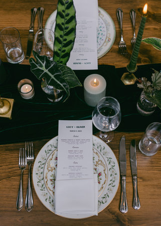 A beautifully arranged dinner table is set for a special gathering, featuring exquisite plates, flickering candles, and an elegant menu printed on fine paper.の写真素材