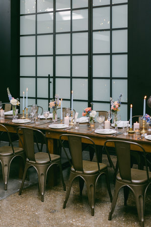A long wooden dining table is set with various dishes, candles, and floral arrangements, creating a warm and inviting atmosphere for guests. Soft lighting enhances the stylish decor.の写真素材