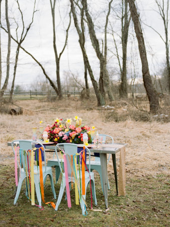 A beautifully arranged outdoor table showcases vibrant flowers and colorful ribbons attached to...