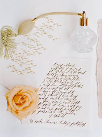 Handwritten notes featuring elegant calligraphy rest on a textured surface beside a vintage perfume bottle and a delicate rose, creating a romantic atmosphere.の写真素材