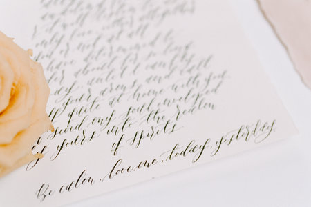 A beautifully penned letter featuring intricate calligraphy lies on a light surface. A soft peach rose sits beside it, creating a tranquil atmosphere perfect for reflective moments.の写真素材
