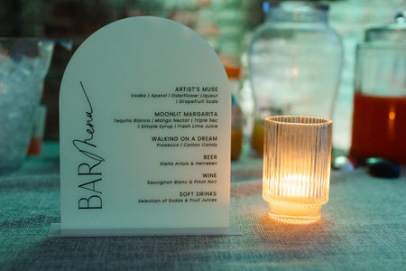The stylish bar menu features a selection of cocktails, wines, and soft drinks, all elegantly presented beside a softly glowing candle, creating a warm atmosphere.の写真素材