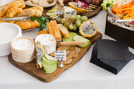 A colorful assortment of cheeses, fruits, and breads is beautifully displayed on a wooden board at a...