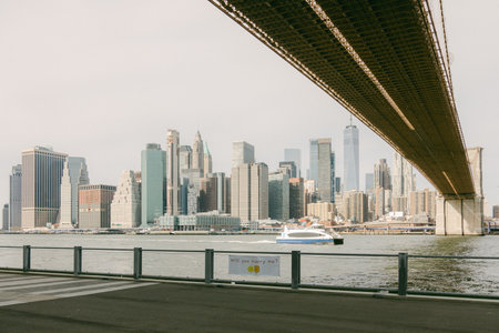 Skyline of New York City from beneath a bridge, highlighting towering skyscrapers and a boat...