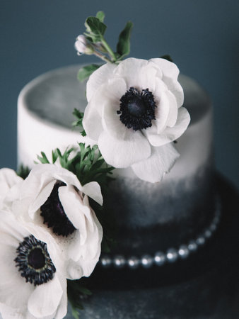 A beautifully designed cake features a black and white gradient and is topped with delicate white flowers. The setting showcases a chic table arrangement that enhances the cake's elegance.の写真素材