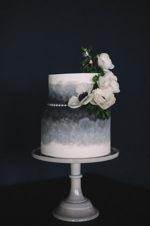 A stunning two-tier cake featuring a gradient gray design adorned with fresh white flowers and...