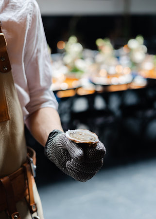 A chef in a white shirt and gloves holds a freshly shucked oyster, ready to serve at a fine dining establishment.の写真素材