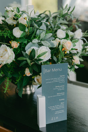 Fresh white roses and green foliage enhance the bar menu displayed on a sleek table in a stylish setting.の写真素材