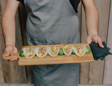 Tasty tacos on a wooden platter with a chef displaying skills in a rustic setting.の写真素材